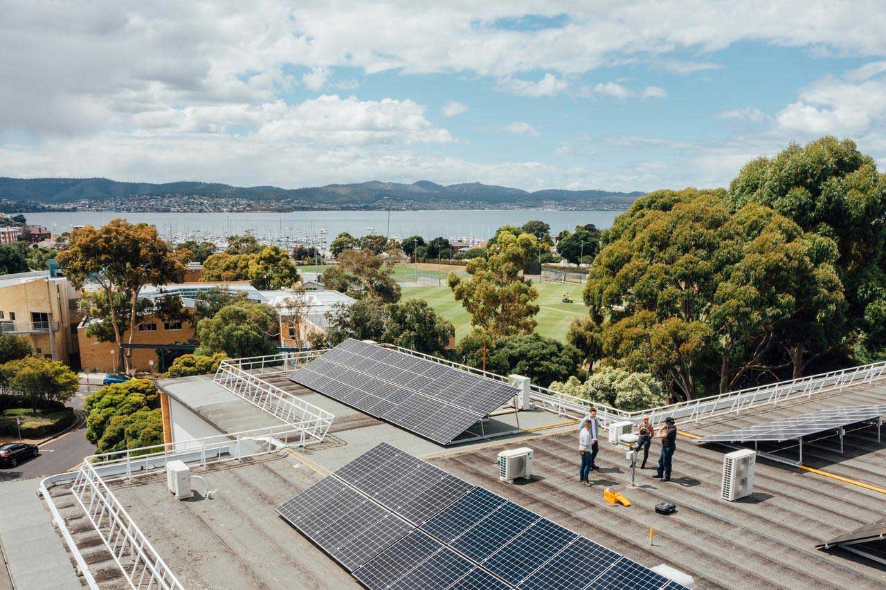 Group inspecting rooftop solar panels on engineering building,  recreation grounds and river Derwent in the background.