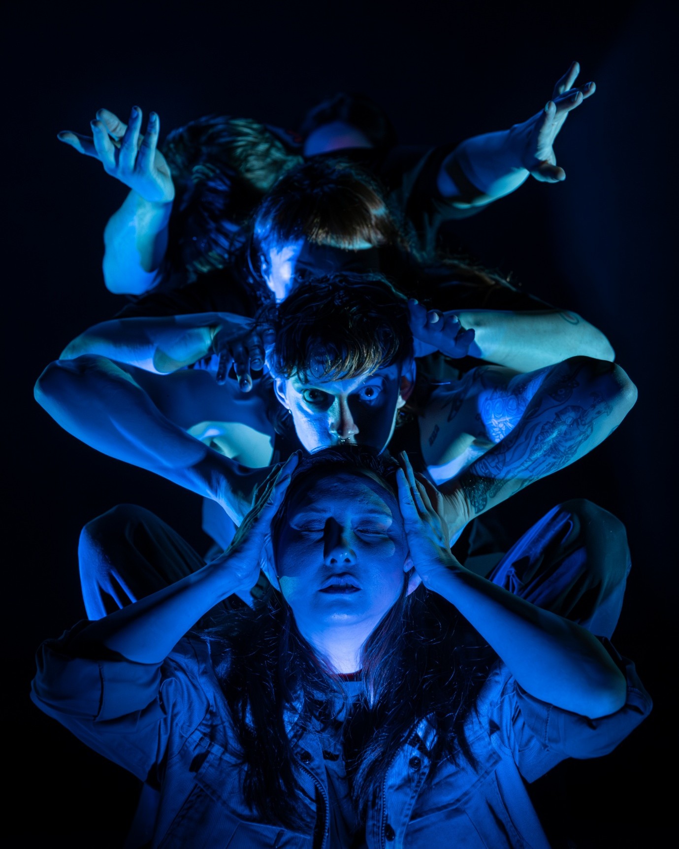 Four people in a row under a blue light, first person with hands on head