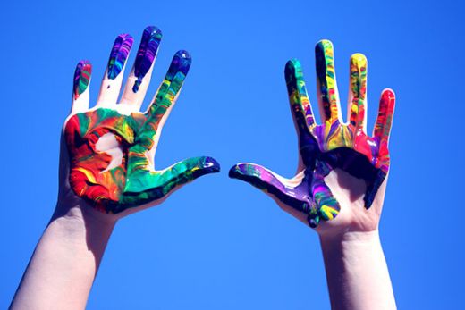 Rainbow painted hands reaching up with blue background.