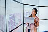 Individual standing in front of a large, multi-panel display screen, holding a sheet of paper.