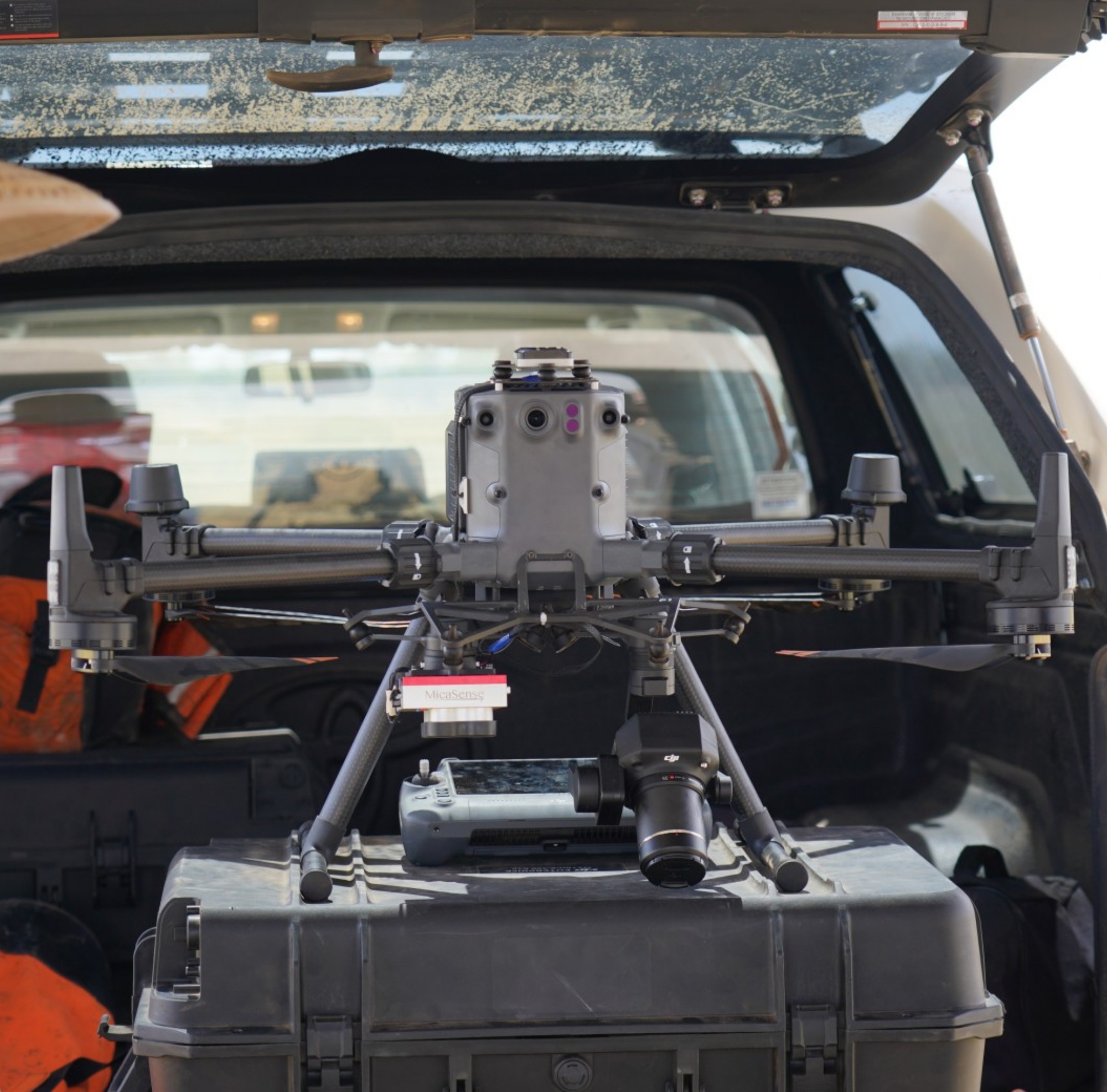 Drone with sensors and camera on a hard case in a vehicle, with gear including an orange vest.
