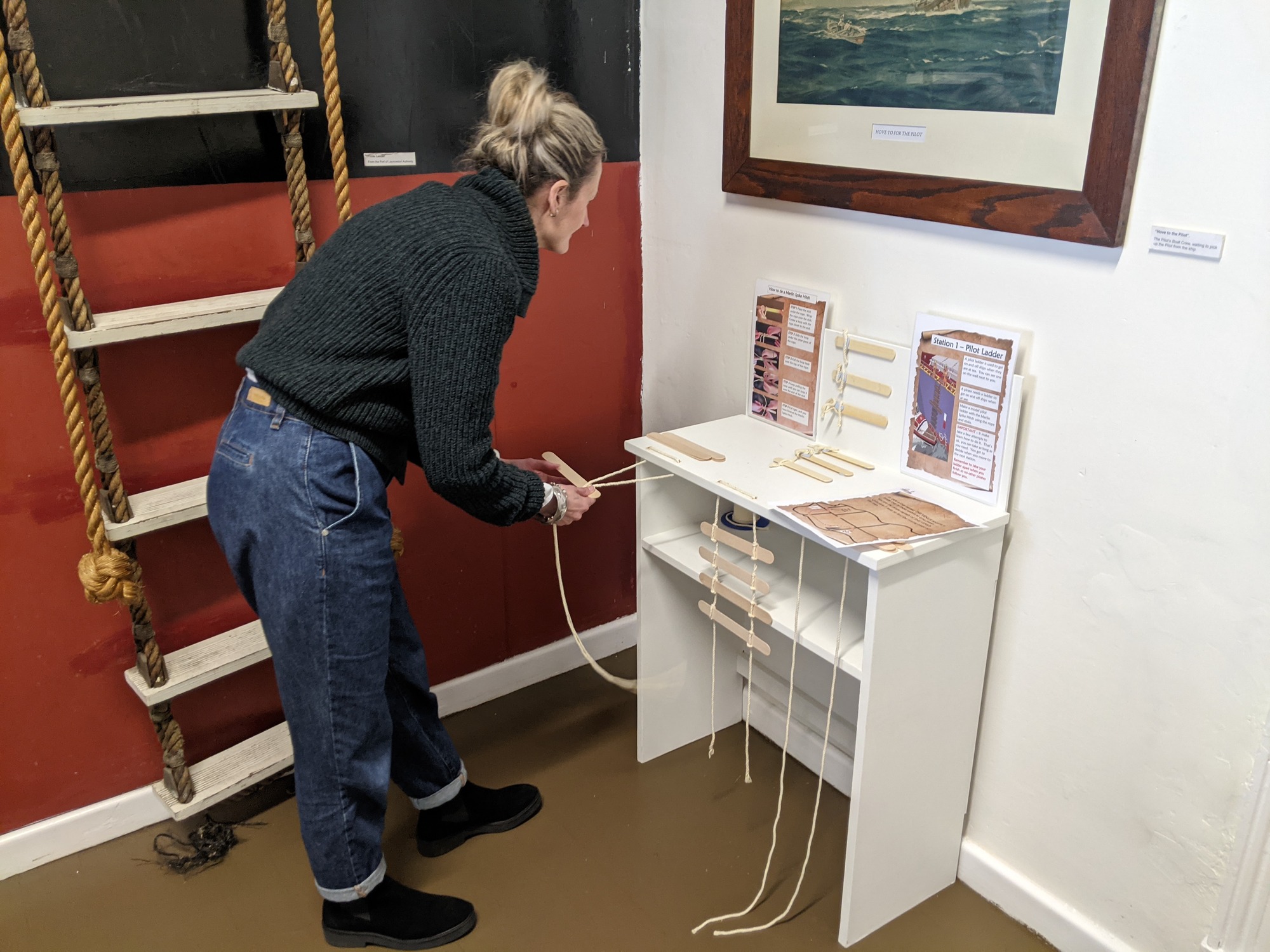 The Deputy Director of the Peter Underwood Centre, Becky Shelley, tests out the pirate map activity at the Low Head Pilot Station Maritime Museum. She is bent over a table with small handmade ladders on it, and is working through instructions on an activity sheet.
