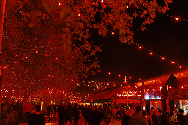 Crowded outdoor setting at Dark Mofo festival Hobart, illuminated by red lights, and food stalls attracting large crowds.