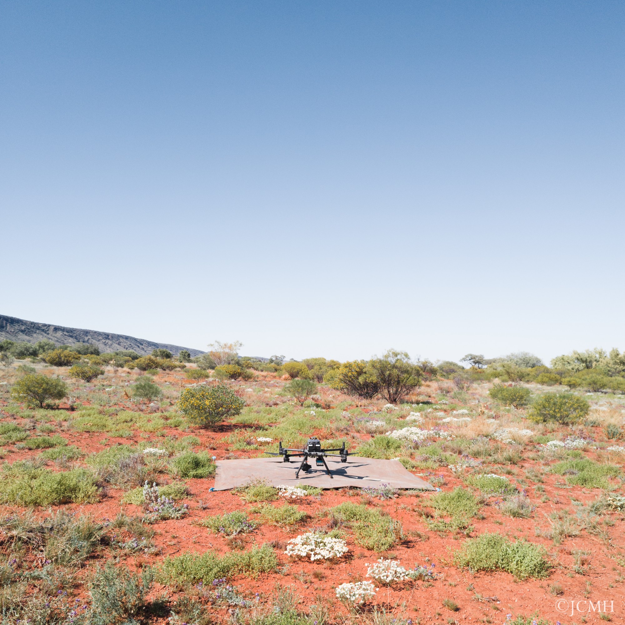 Drone on a mat in a desert landscape with sparse bushes, hills, and a clear blue sky.