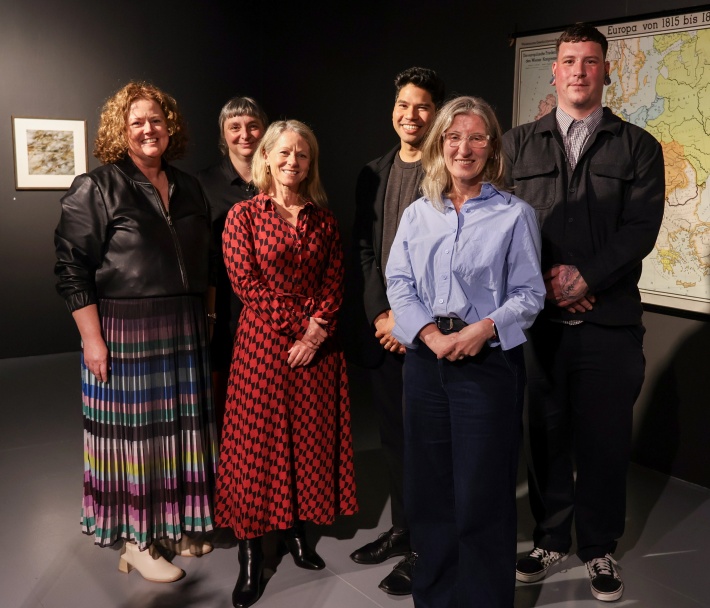 Four women and two men standing in a black walled gallery