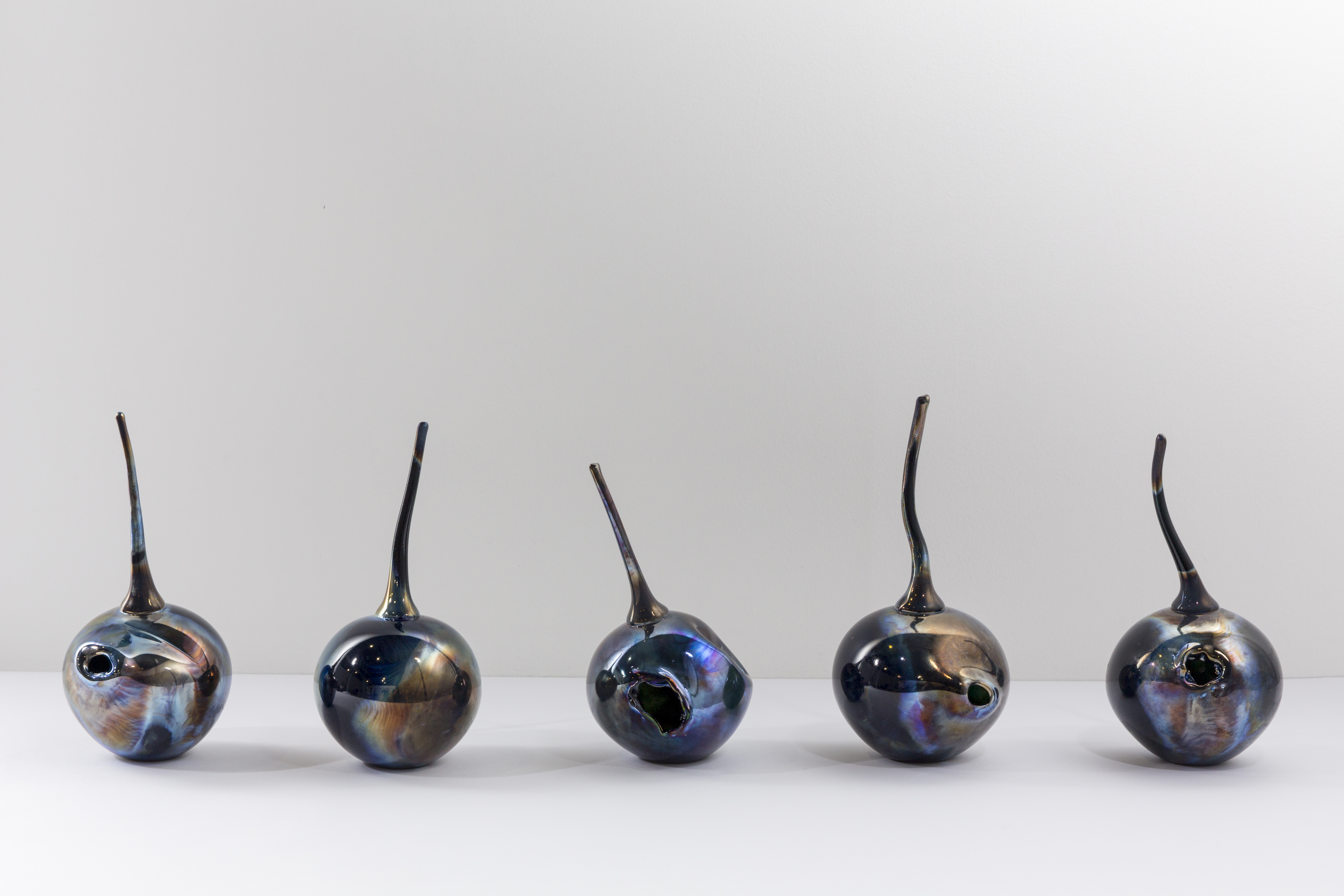 Image Description: A photograph of five glass cherry-like objects resembling bush plums. They sit on a white plinth against a white background. 