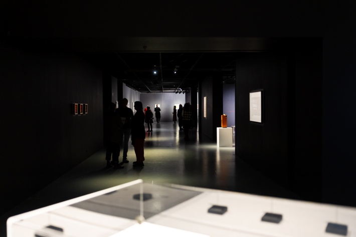 Long view of a darkened gallery with exhibits spotlit and people in shadow
