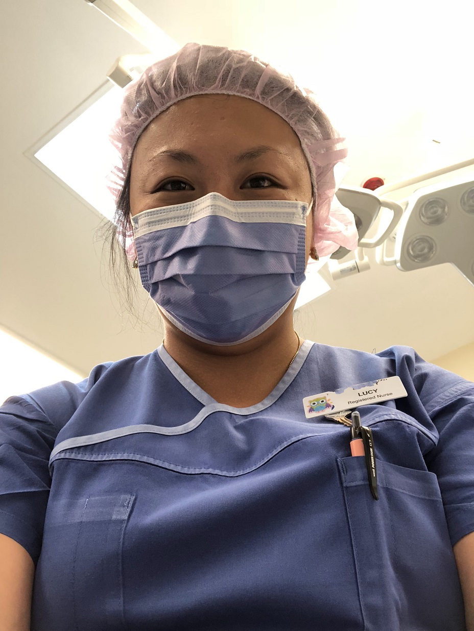 Tasmanian Registered Nurse Lucy Gardam smiles from behind her surgical mask, wearing her scrubs and a name badge. (Picture: supplied by Lucy Gardam)