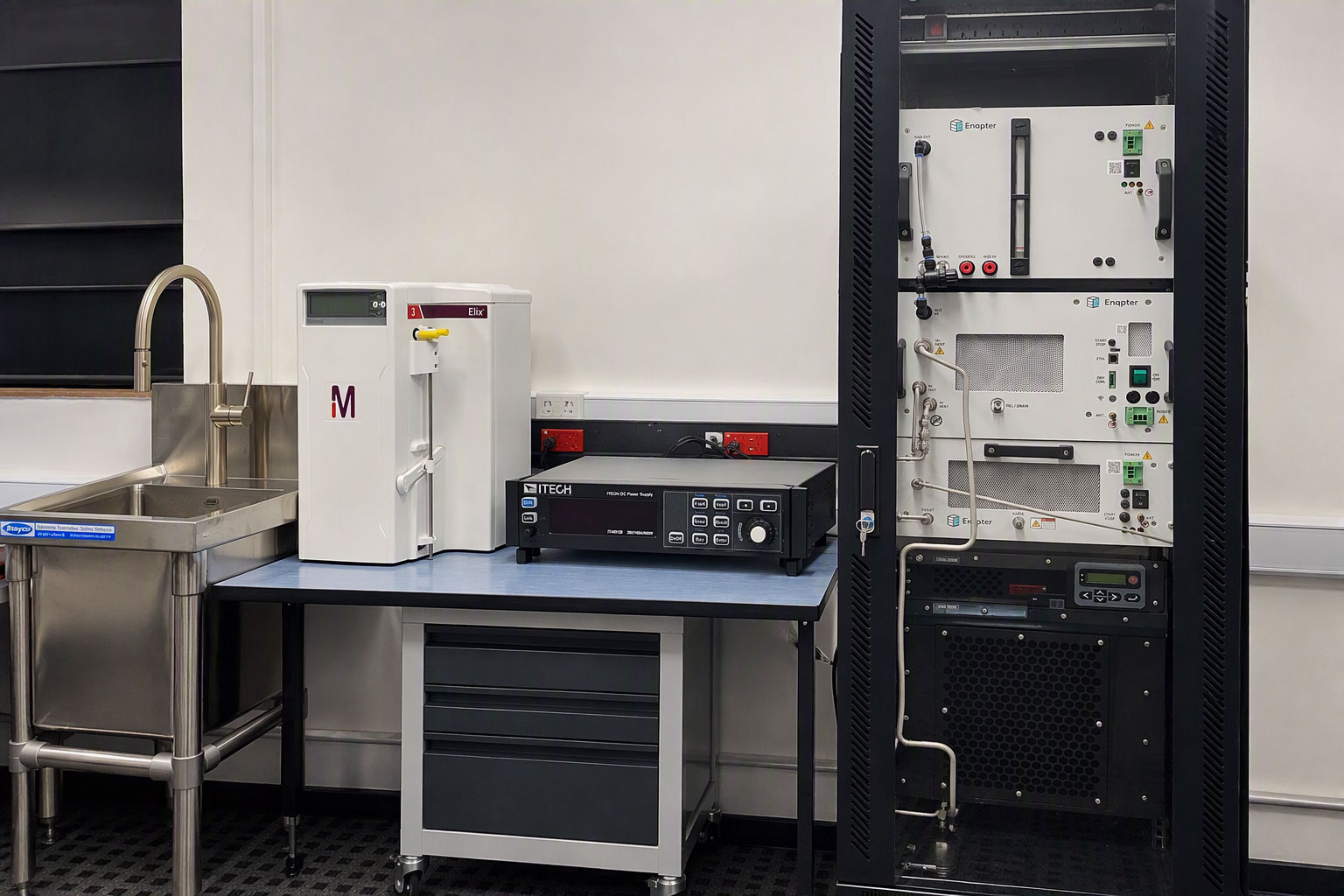 Hydrogen analysis equipment, including a benchtop instrument and gas analysis system housed in a tall equipment rack next to a stainless-steel sink.