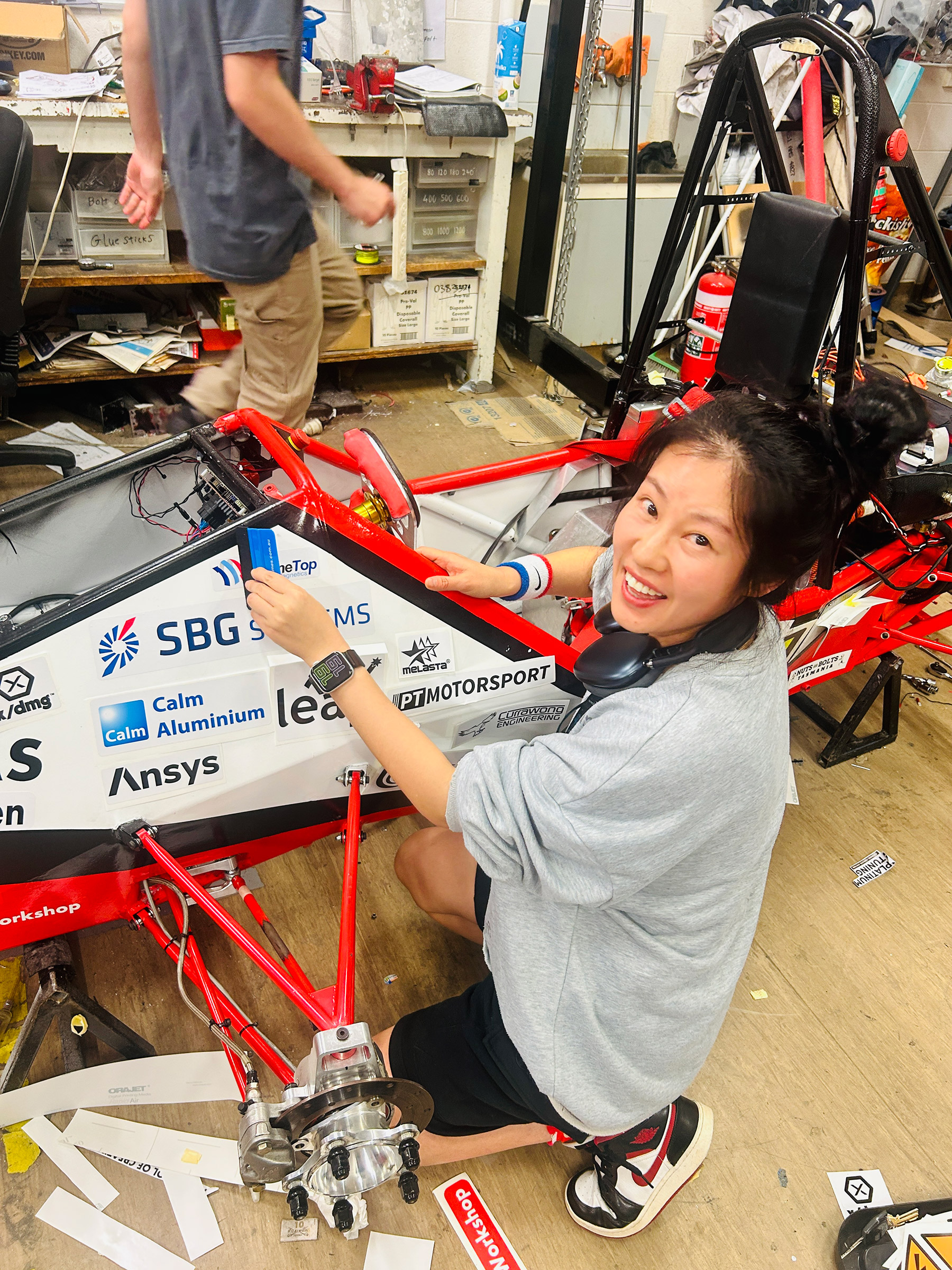 Luoyan applying sponsor decals to a red formula-style race car chassis in a workshop.