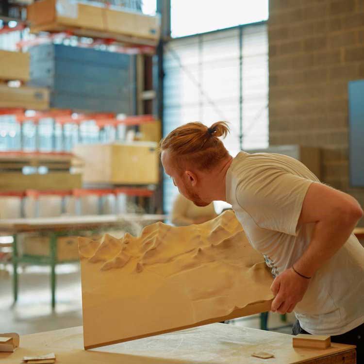 A person in a workshop examining a large, intricately carved wooden panel.