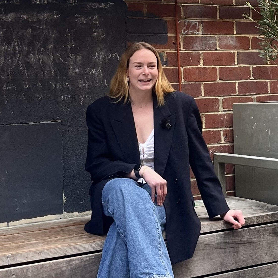 Belle Smith sitting on a wooden bench against a brick wall facing an interview.