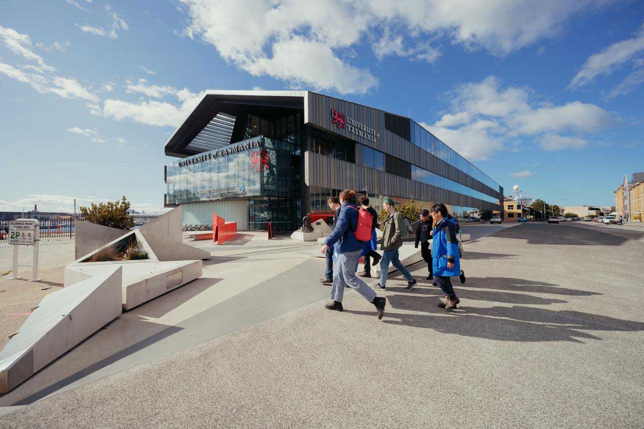 Several individuals walking past in towards the IMAS building under a partly cloudy sky.