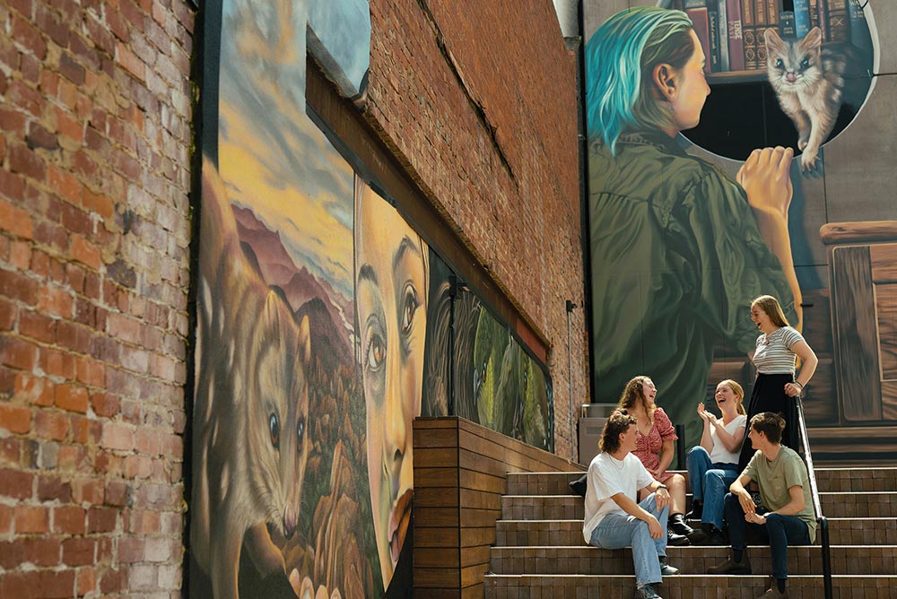 University of Tasmania scholarships recipients talking in front of the George Alexander mural in Hobart city