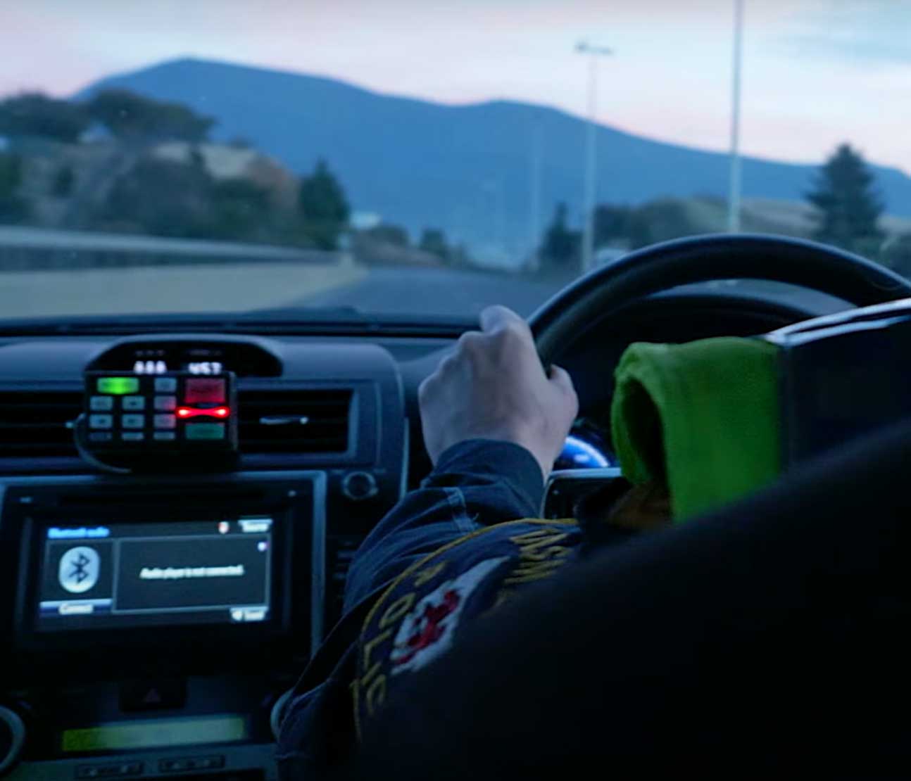 Law enforcement officer driving a car with a view of the dashboard and a mountainous landscape ahead.